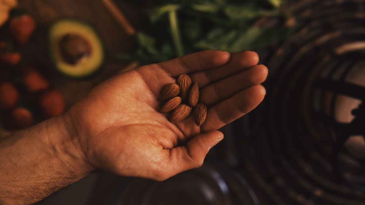 Top view of crop hand with pile of raw unpeeled almonds above table with ingredients